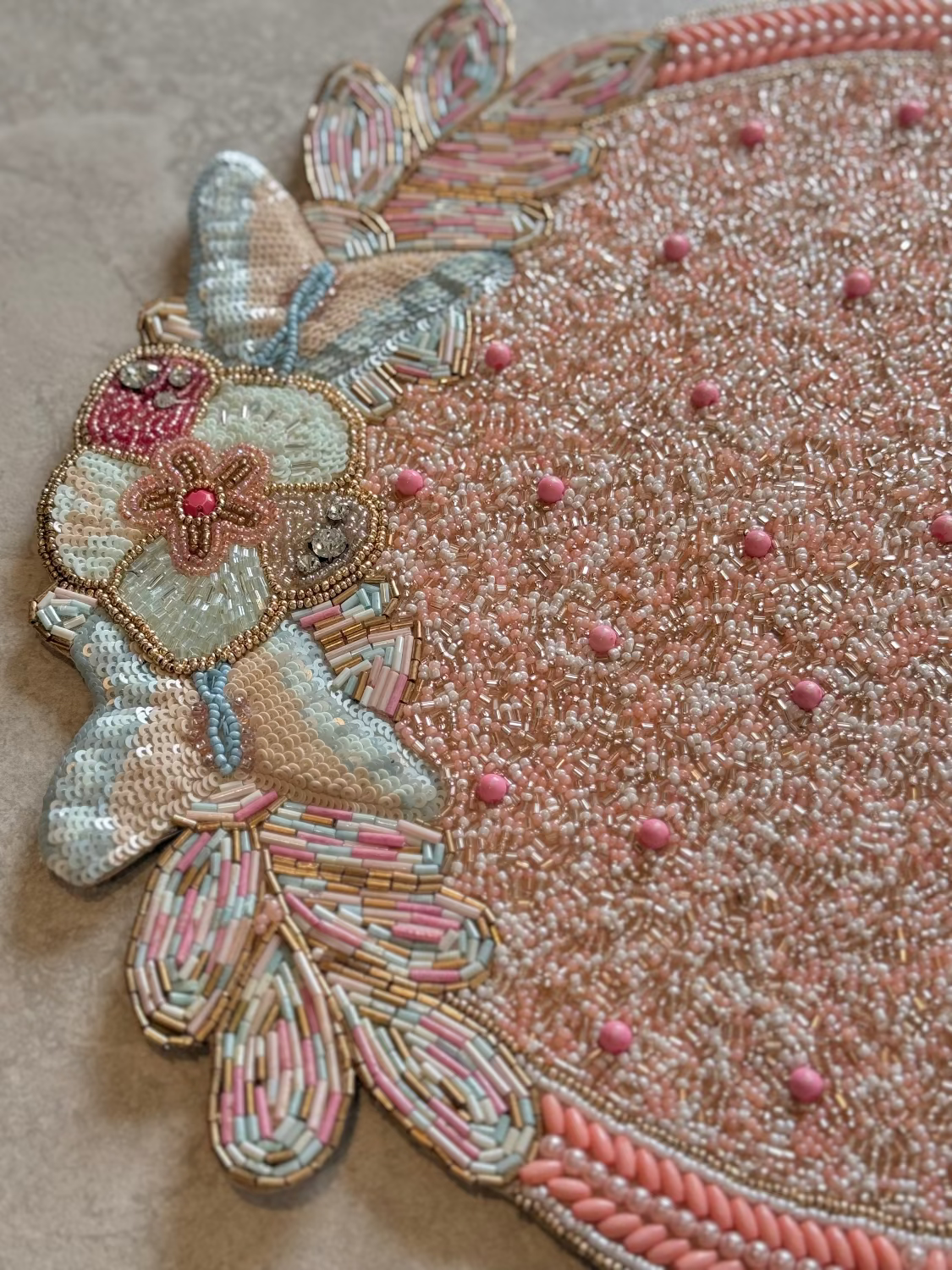 Close-up of an intricately beaded and embroidered butterfly design on a textured surface.