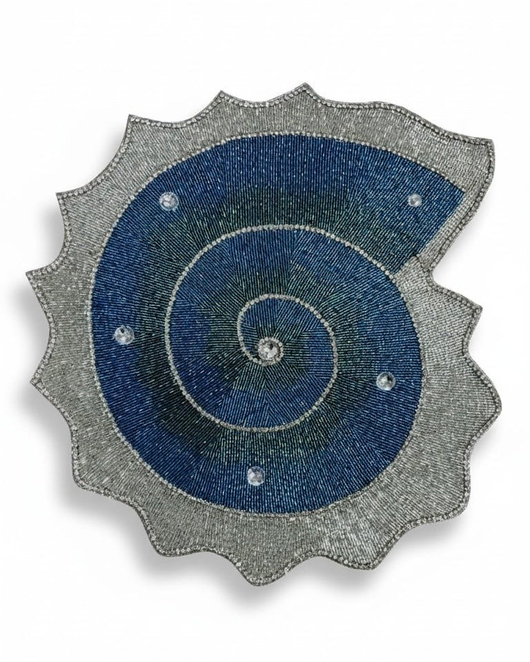 Handmade beaded decorative placemat in the shape of a shell with blue spiral design and silver rhinestone embellishments 